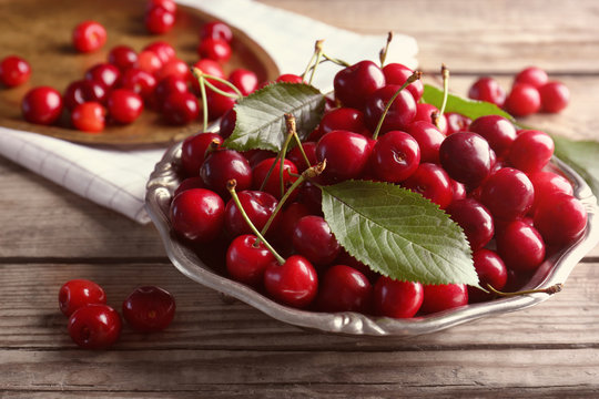 Plate with sweet cherries on wooden background