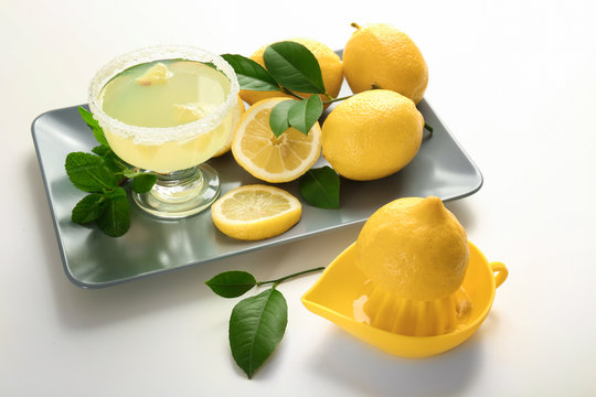 Platter with glass of juice, lemons and squeezer on white background