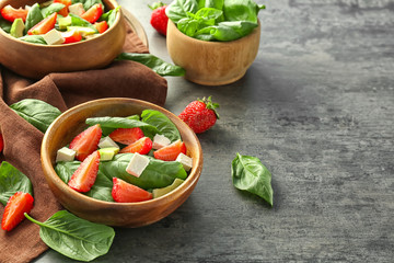 Bowls of salad with spinach leaves, strawberry and cheese on table