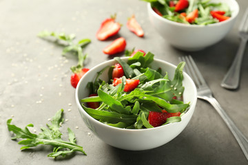 Bowl with tasty strawberry arugula salad on table