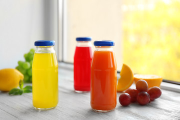 Delicious juices in bottles and fruits on window sill