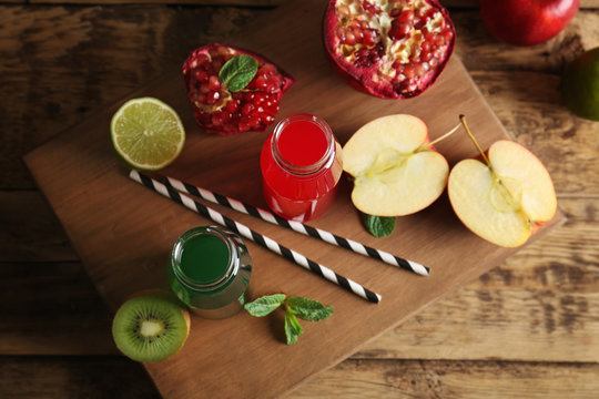Delicious juices in bottles and fruits on wooden board