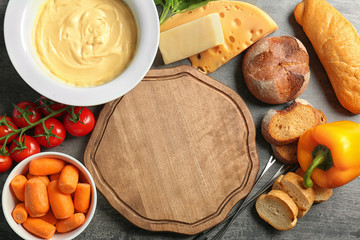 Plate with cheese fondue and different products around cutting board on table