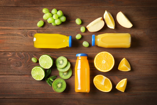 Delicious juices in bottles and fruits on wooden background
