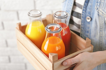 Young woman holding wooden crate with delicious juices in bottles