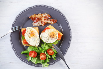 Plate with delicious egg sandwiches, vegetables and beacon on light table