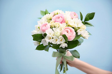 Female hand holding beautiful bouquet with white freesia on light background