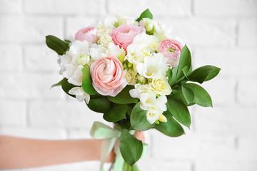 Female hand holding beautiful bouquet with freesia flowers on white brick wall background