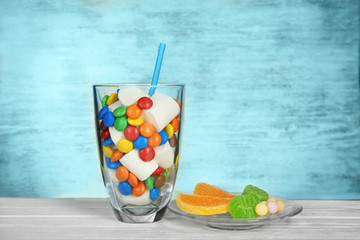 Glass with marshmallows and candies on wooden table
