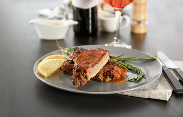 Plate with delicious pork ribs, lemon slices and rosemary on table