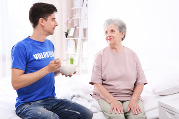 Obraz premium Young male volunteer feeding elderly woman in light room