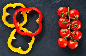 Tomatoes on a branch with bell pepper slices on a dark background