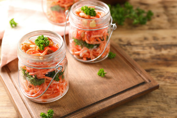 Jars with delicious carrot raisin salad on wooden background