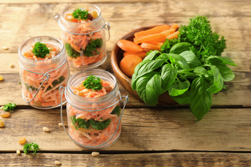 Jars with delicious carrot raisin salad on wooden background