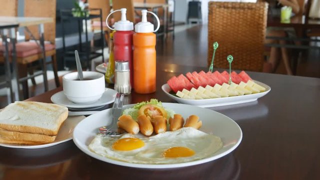 Panning shot of American breakfast with sunny side up eggs, toast, coffee and  fruit in restaurant