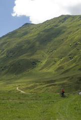Mountain summer landscape: path with an electric bicycles E-bike on a sunny day, with clouds and as a backdrop of mountain pastures of fresh grass, Belalp, Alps, Switzerland