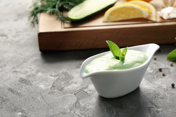 Delicious yogurt sauce in gravy boat with ingredients on grunge background