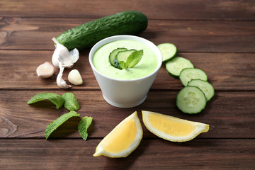 Delicious yogurt sauce in bowl with ingredients on wooden background