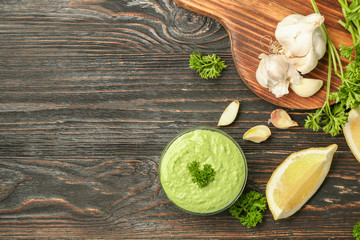 Delicious yogurt sauce in bowl with ingredients on wooden background