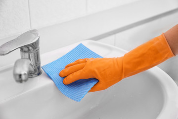 Female hand with sponge cloth cleaning a sink in the bathroom
