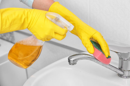 Woman cleaning tap with sponge and detergent in bathroom