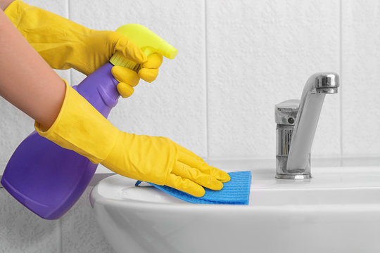 Woman cleaning sink with sponge cloth and detergent in bathroom