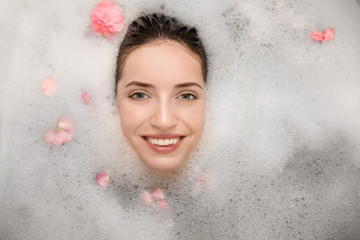 Woman relaxing in bath with foam and petals. Spa treatment concept