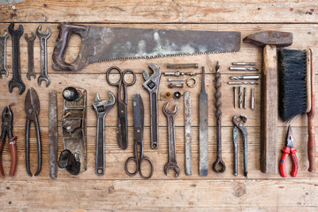 Composition of construction tools on an old battered wooden surface of tools: pliers, pipe wrench, screwdriver, hammer, metal shears, saws.