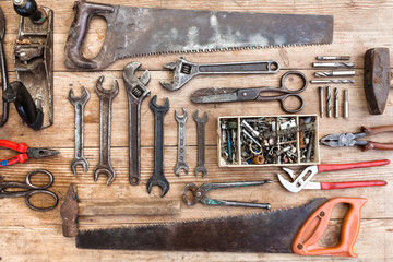 Composition of construction tools on an old battered wooden surface of tools: pliers, pipe wrench, screwdriver, hammer, metal shears, saws.