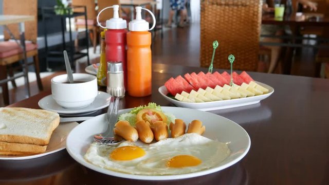 Panning shot of American breakfast with sunny side up eggs, toast, coffee and  fruit in restaurant
