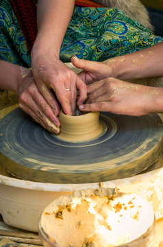 The hands of a teacher who teaches a student how to make pottery from clay on a potter's wheel