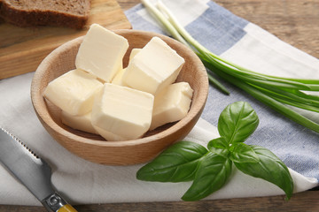 Bowl with cubes of butter and greens on table