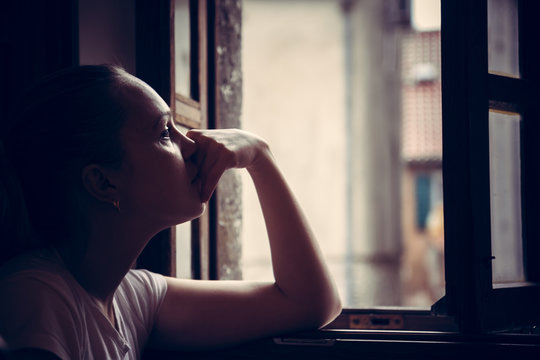 Pensive Thoughtful Young Woman Lost In Thoughts Dreaming And Looking In Opened  Window In Vintage Style With Dramatic Mood 