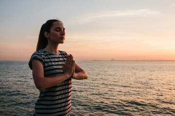 Young beautiful girl practicing yoga and meditation on the rocks next to the sea at sunset. Sport. Yoga. Meditation. Recreation. Vacation. Relaxation.