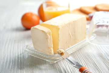 Piece of butter in dish and knife on wooden table