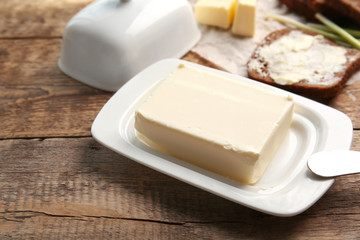 Piece of butter in dish, knife and delicious toast on wooden table