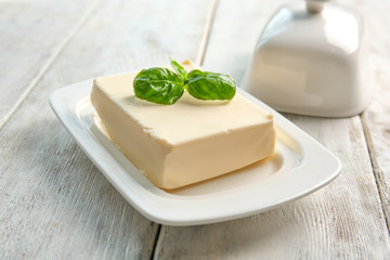 Piece of delicious butter and basil leaves in dish on wooden table