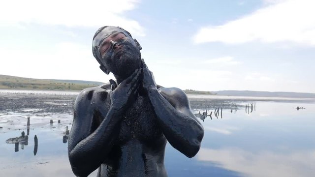 Young Man Making Face Mask with Black Medical Mud at the Lake of Salt Water. Salty Black Dirt Is Good For People With Health and Skin Problems. HD Slowmotion.