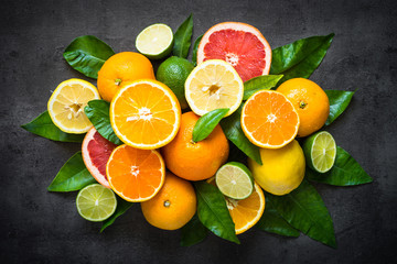 Fresh citrus fruit assortment on black. Whole and sliced fruit top view. Food background.