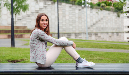 Beautiful young trendy woman sitting with her legs up on a park bench