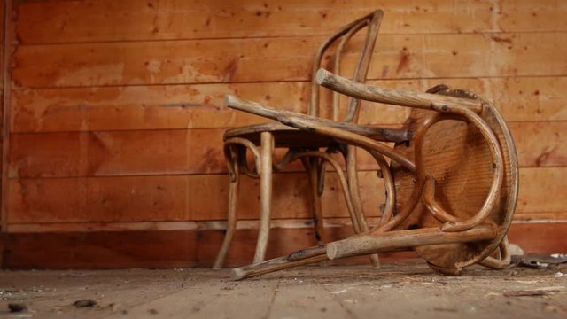 Old wooden chairs sit on the floor of an abandoned wooden cabin.