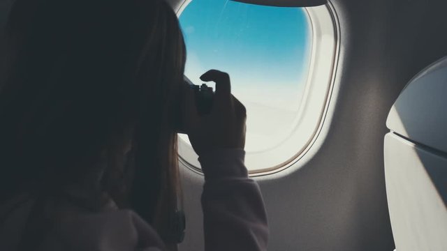 Young Caucasian female taking pictures with her film camera through the airplane window during flight. 4K UHD