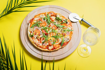 Pizza and glass of white wine on wooden board on yellow tropical background