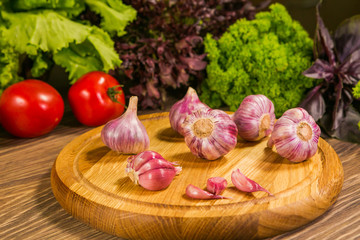 Garlic bulbs on a wooden board with a green salad in the background. Delicious vegetarian food