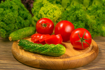 Fresh vegetables. Tomatoes and cucumbers on a wooden table. Green salad in the background.