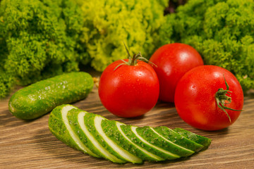 Fresh vegetables. Tomatoes and cucumbers on a wooden table. Green salad in the background. Healthy food,dieting consept.
