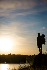 Fototapeta premium Young tourist with backpack standing on a rock and enjoying sunset