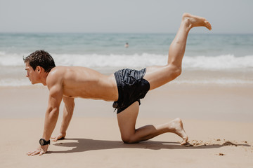 Fototapeta na wymiar Athlete performing exercises on beach in the sun. Young man training in the beach