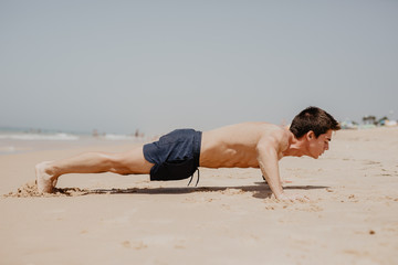 fitness man exercising push ups smiling happy. Male fitness model cross-training on beach.