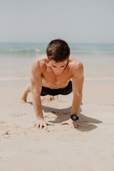 fitness man exercising push ups smiling happy. Male fitness model cross-training on beach.